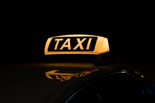 Panneau TAXI  jaune illuminé sur un véhicule sombre la nuit.