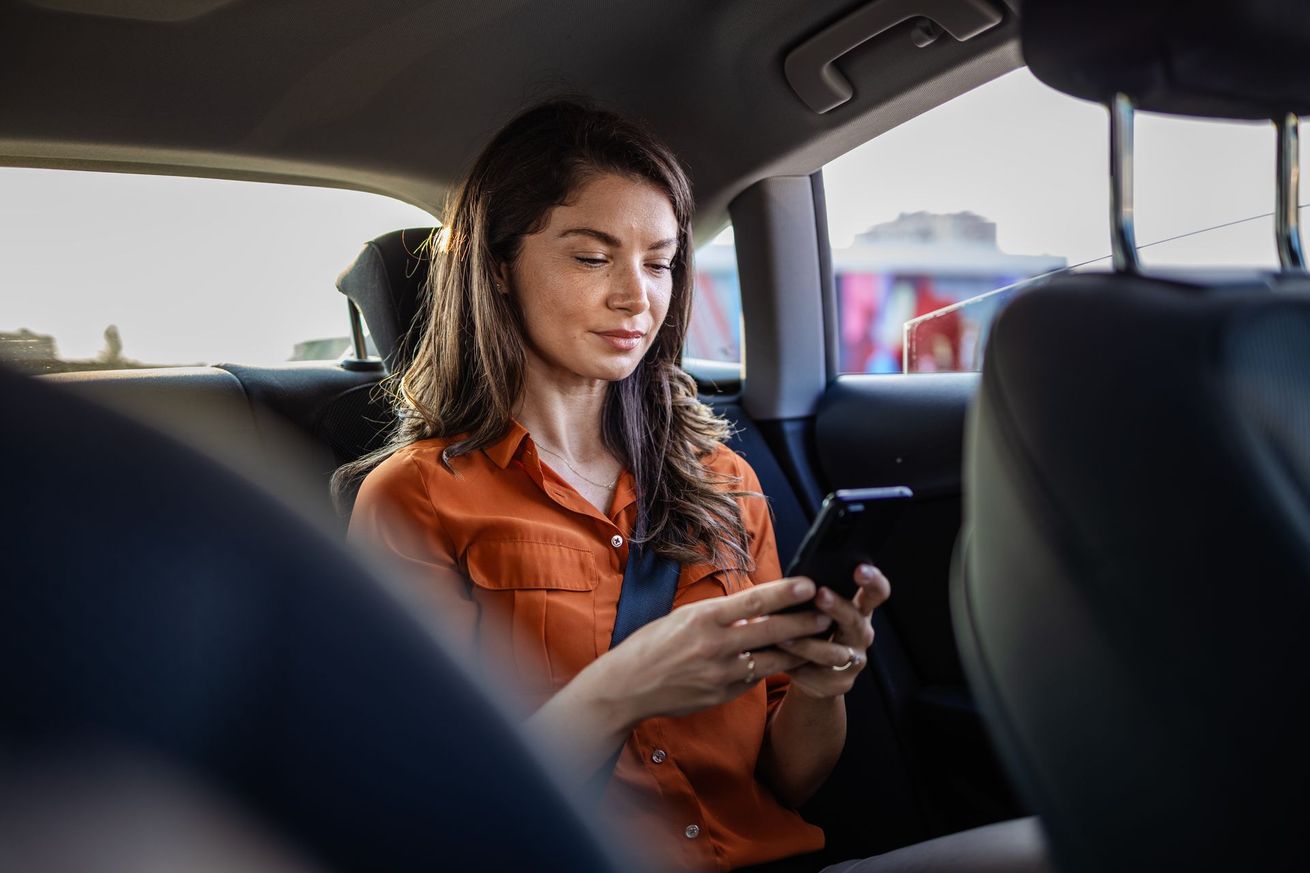 Une femme en chemise orange utilise un Smartphone sur le siège arrière d'une voiture.