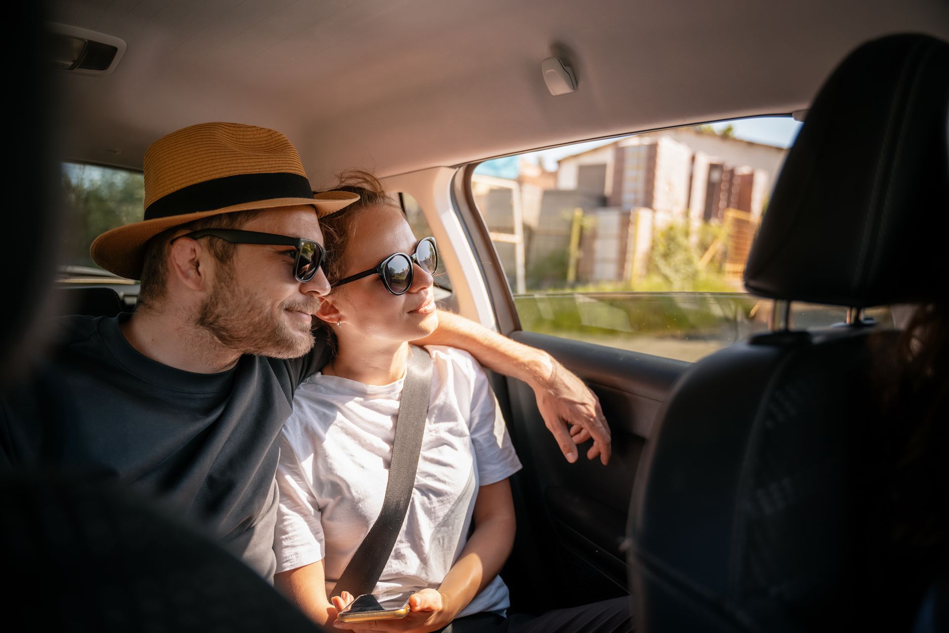 Deux personnes portant des lunettes de soleil, souriantes et regardant par la fenêtre, sont assises dans une voiture.