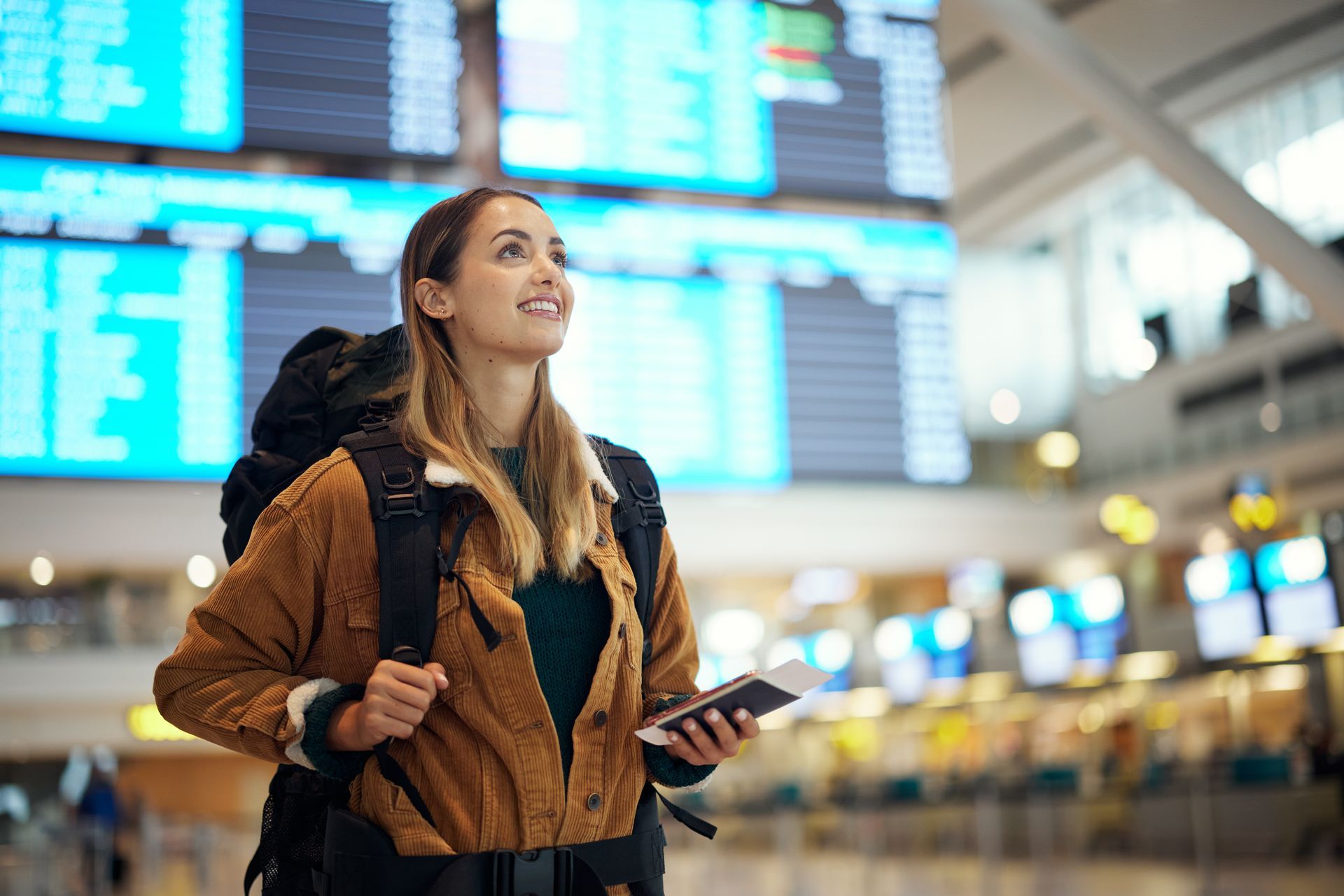 Voyageur avec un sac à dos dans un terminal d'aéroport, avec des panneaux d'information des vols en arrière-plan.