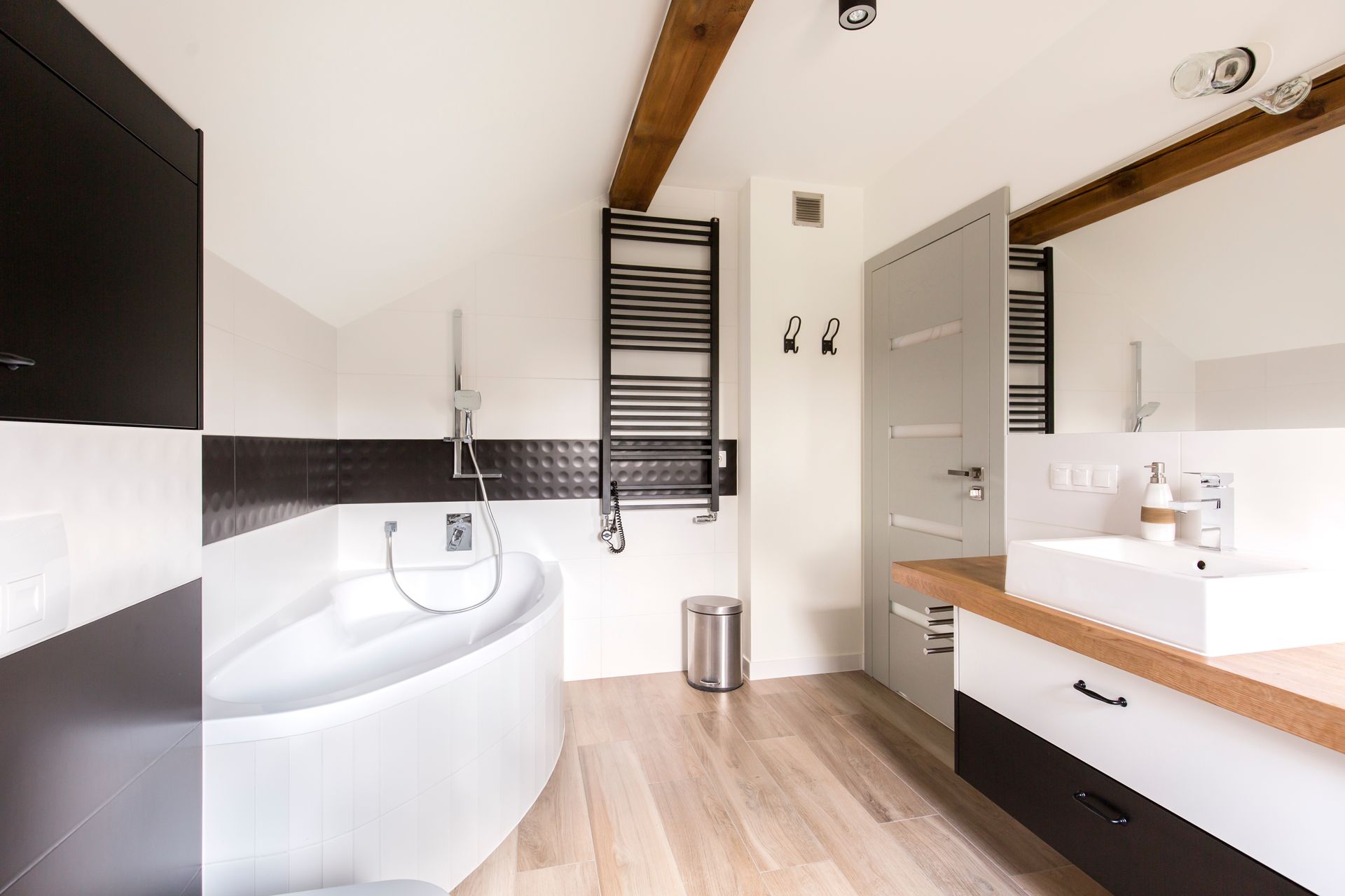 Salle de bains moderne avec baignoire îlot, meuble-lavabo double vasque, miroir et plafond à poutres apparentes.