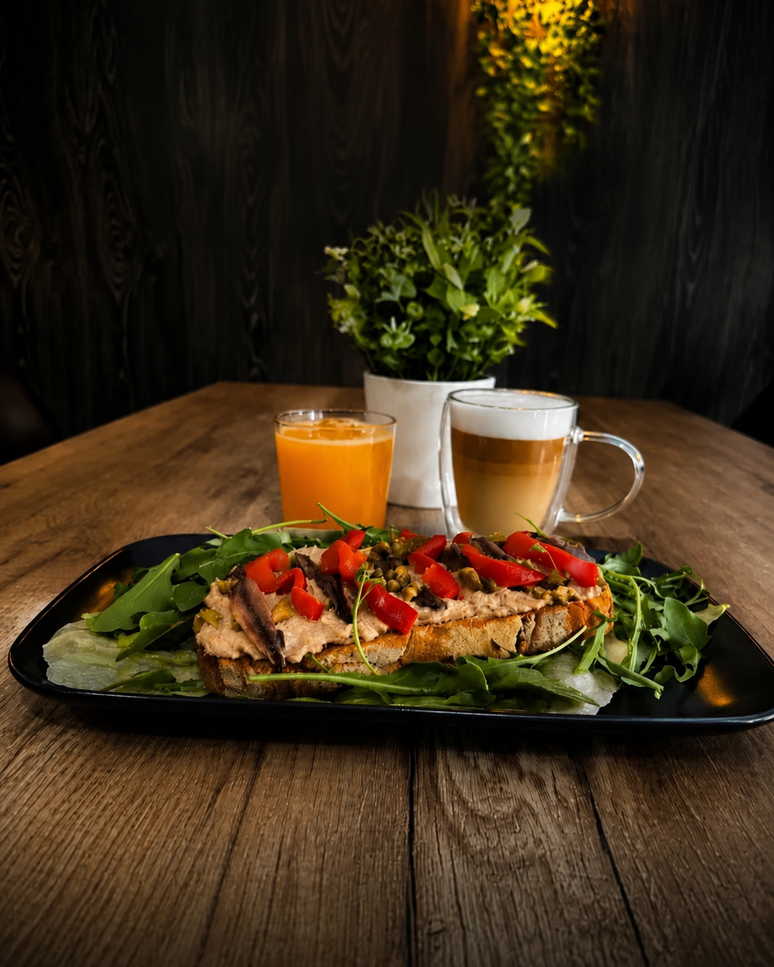 Ensalada de pollo a la parrilla con tomates en un plato negro, con jugo de naranja y café en una mesa de madera.