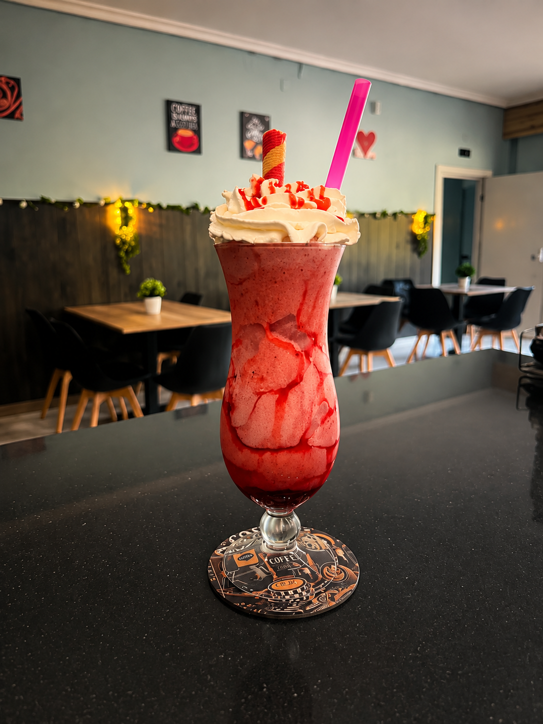 Bebida de postre roja alta, coronada con crema batida y cerezas, sobre la barra de un restaurante.