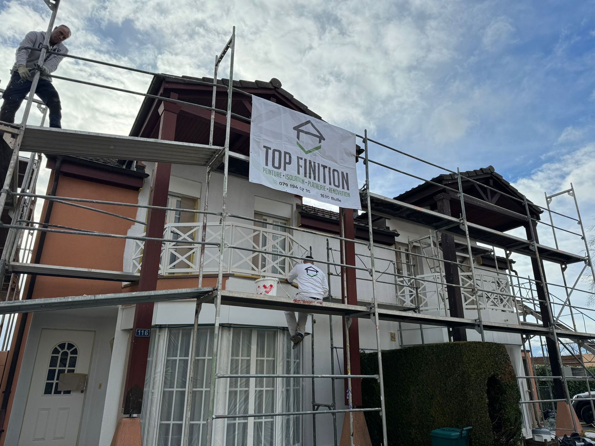 Un homme se tient debout sur un échafaudage devant une maison.