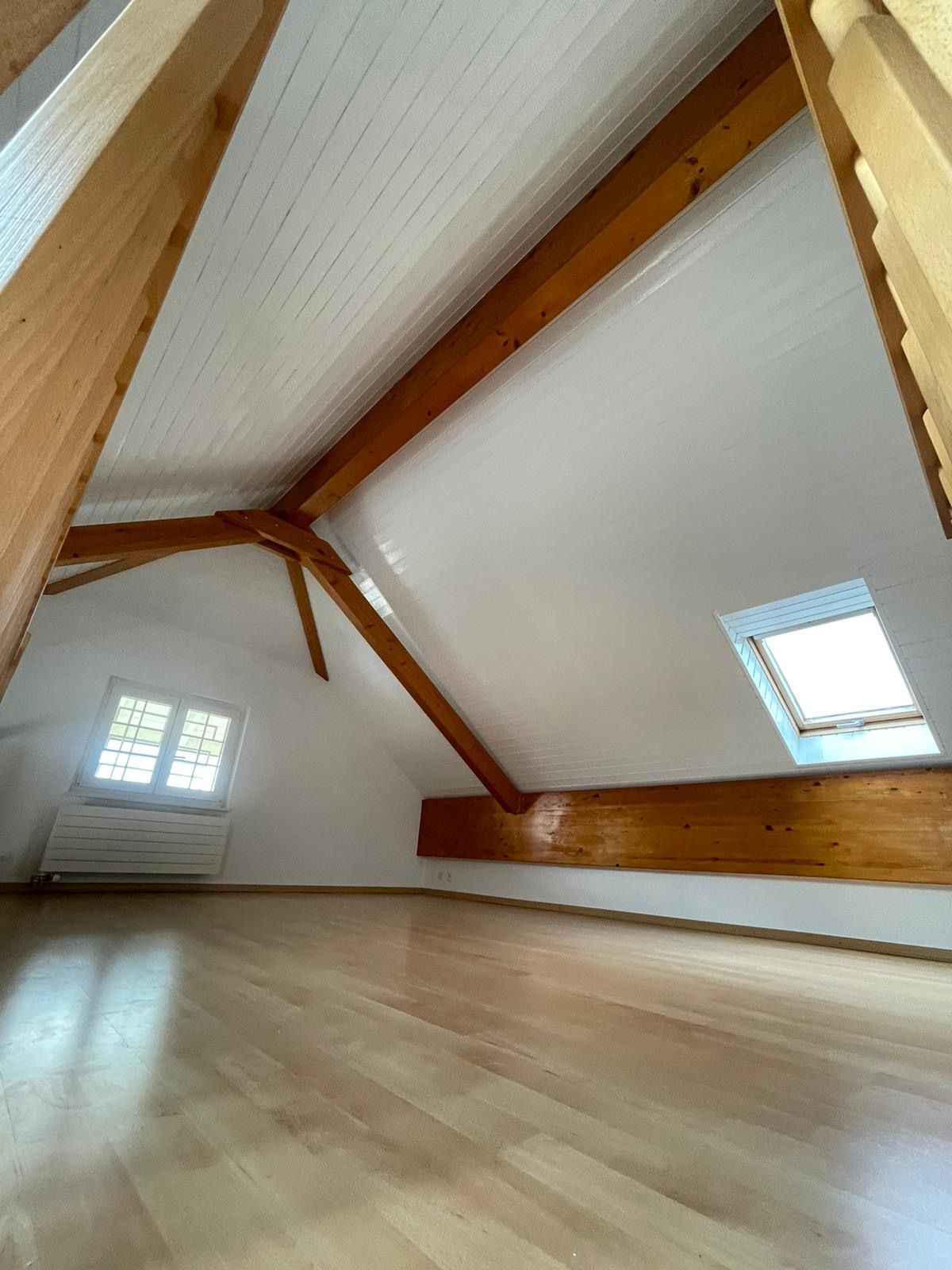 Un grenier vide avec des poutres en bois et une fenêtre.