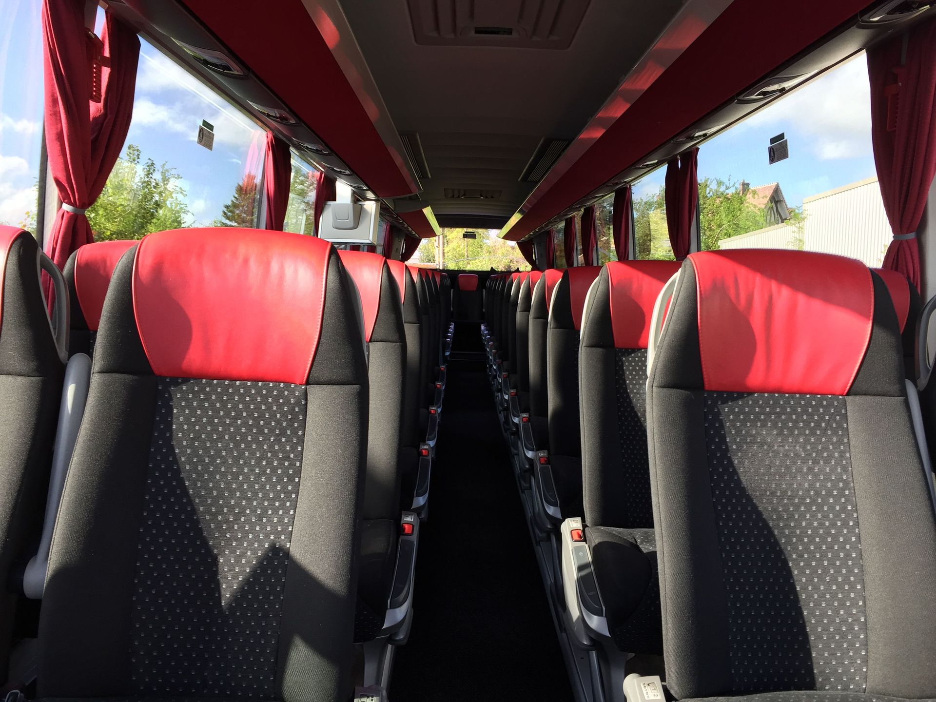 L'intérieur d'un bus avec des rangées de sièges dotés d'appuie-têtes en cuir rouge et de coussins en tissu noir à motifs.