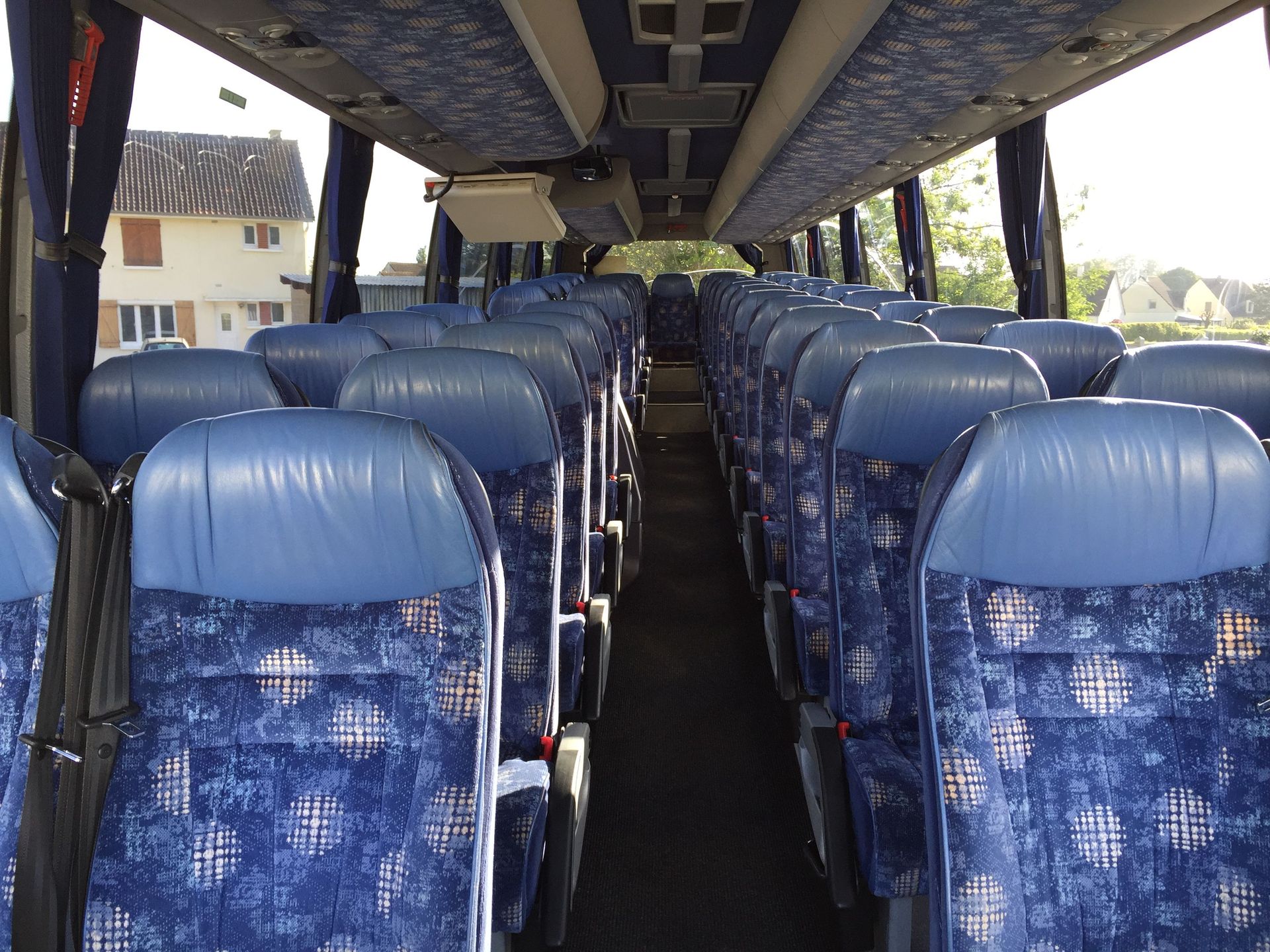 Vue intérieure d'un bus avec des sièges en tissu bleu à motifs disposés en rangées de part et d'autre d'une allée centrale.