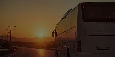 Un autobus de passagers circulant sur une route dégagée au coucher du soleil, avec des montagnes se détachant en arrière-plan.
