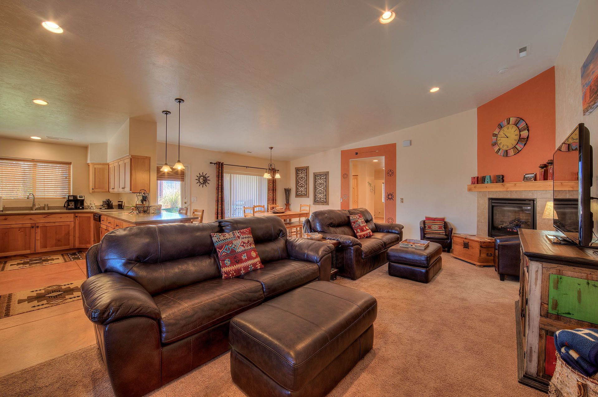 Oleander Place Moab vacation rental Living room with brown leather sofa and ottoman, fireplace, and open kitchen.