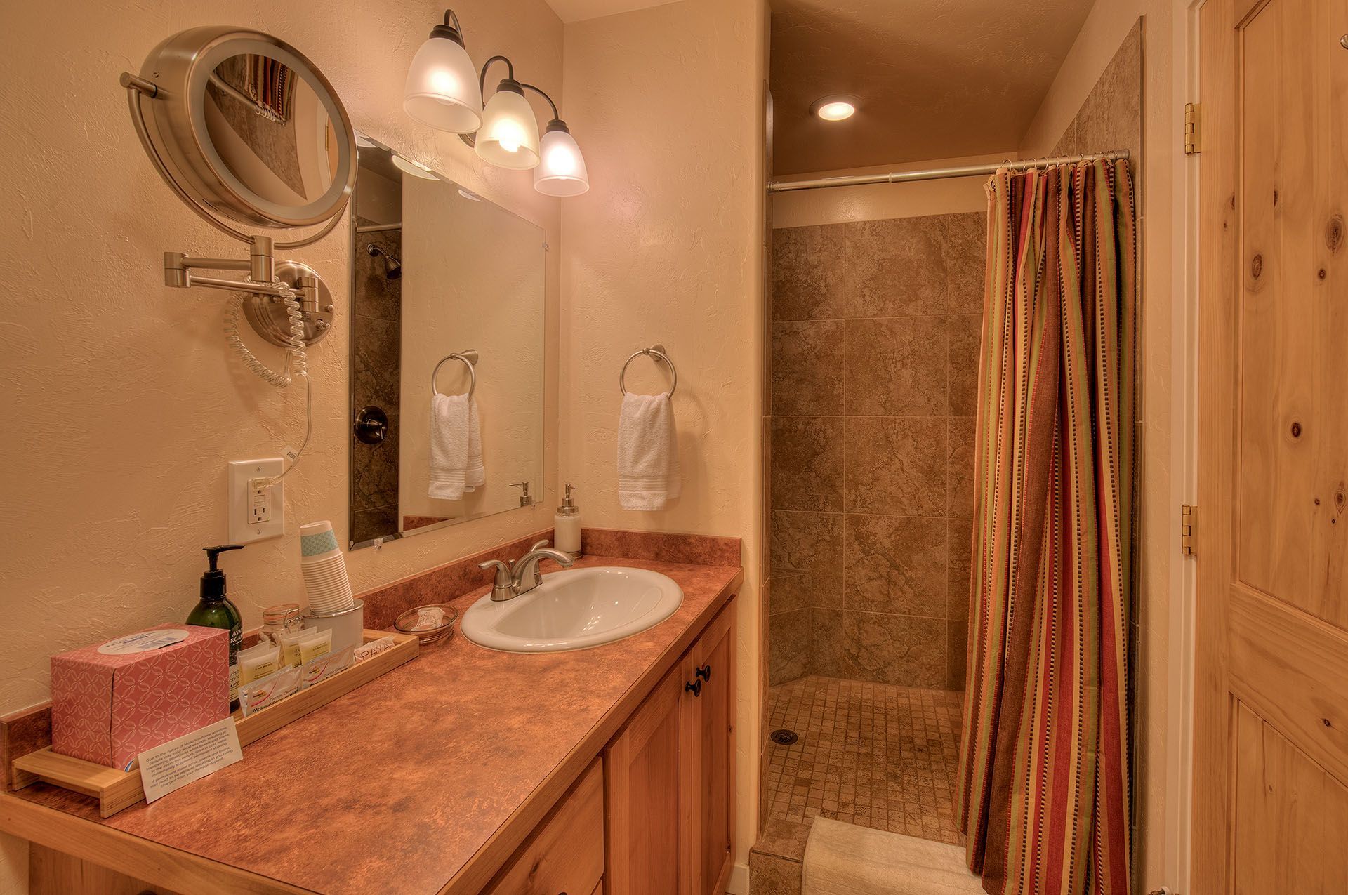 Moab, Utah Oleander Place vacation rental Bathroom with wood vanity, shower, and mirror. White walls, and red countertop.