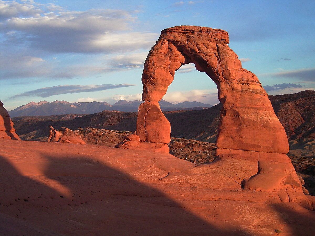 A large rock formation in the Moab, Utah desert with mountains in the background