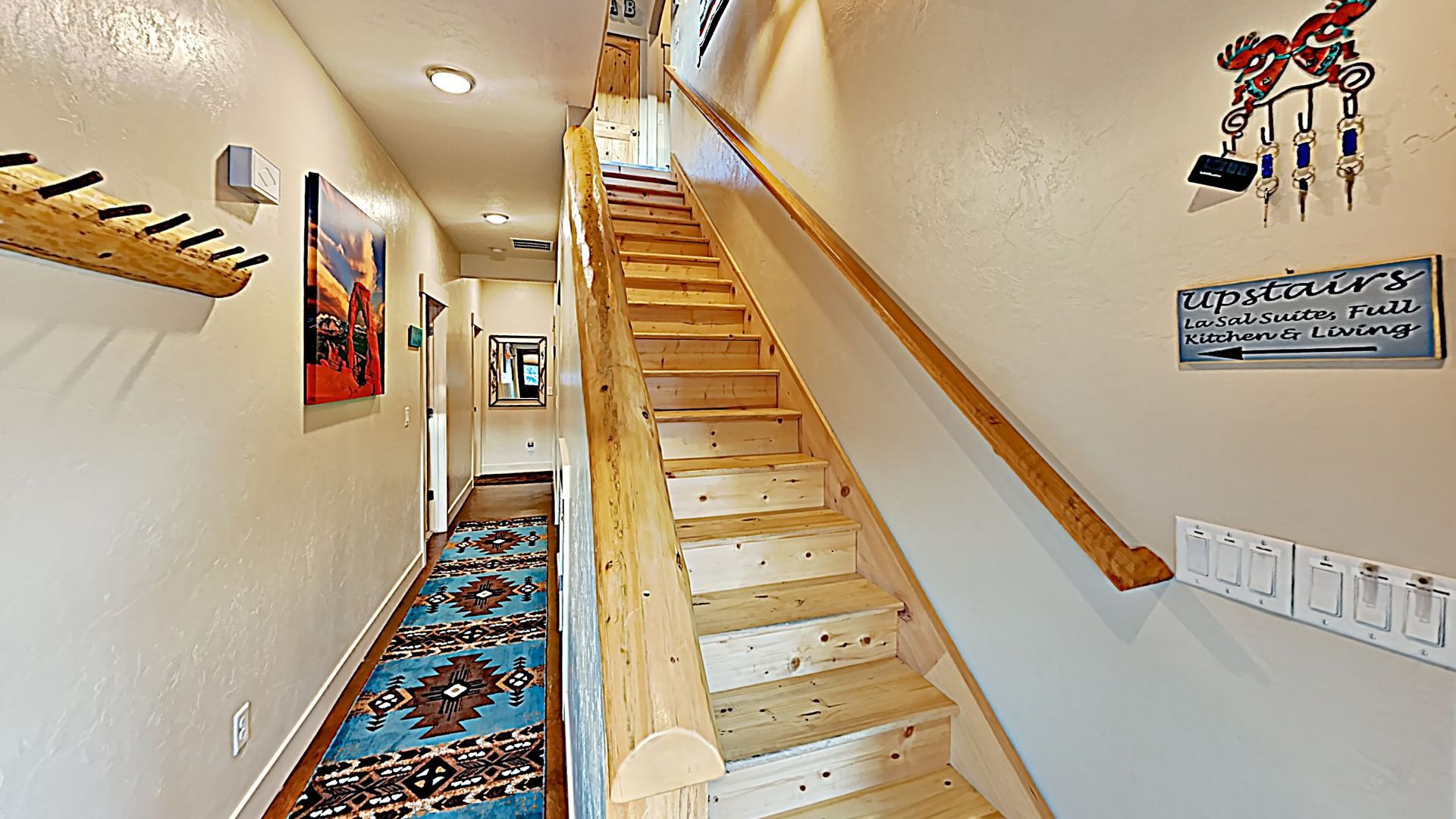 Village Place Moab vacation rental hallway with stairs, colorful rug, coat rack, and keys.