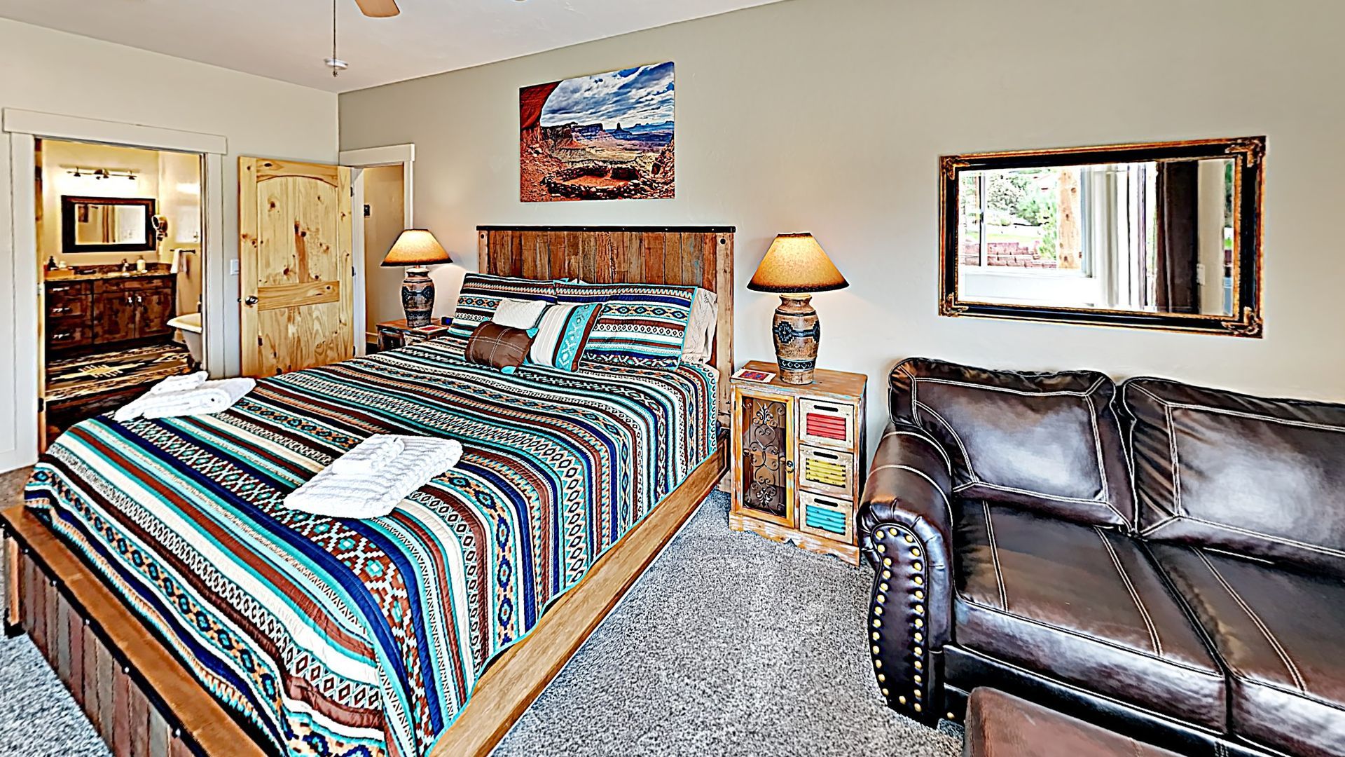 Village Place Moab vacation rental Bedroom with king bed, brown leather sofa, rustic decor.