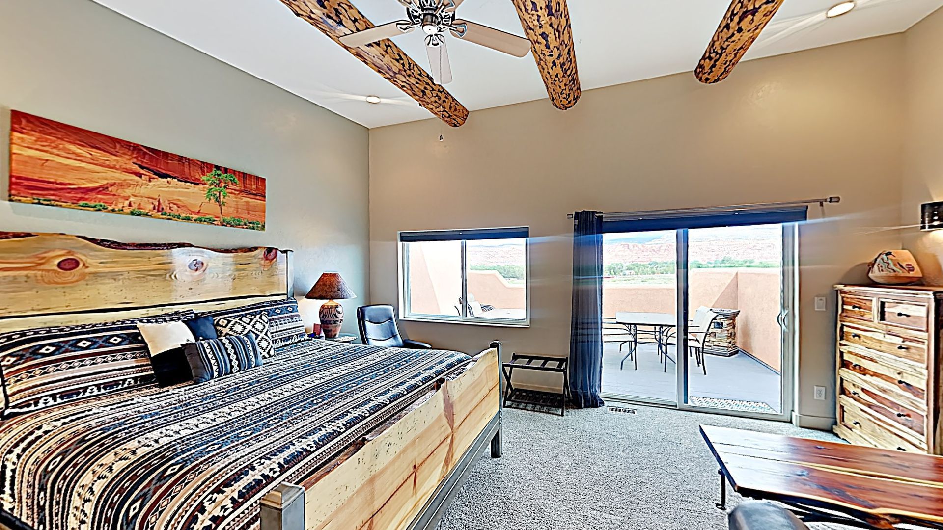 Village Place Moab vacation rental Bedroom with rustic wooden bed, sliding door to patio, and art.
