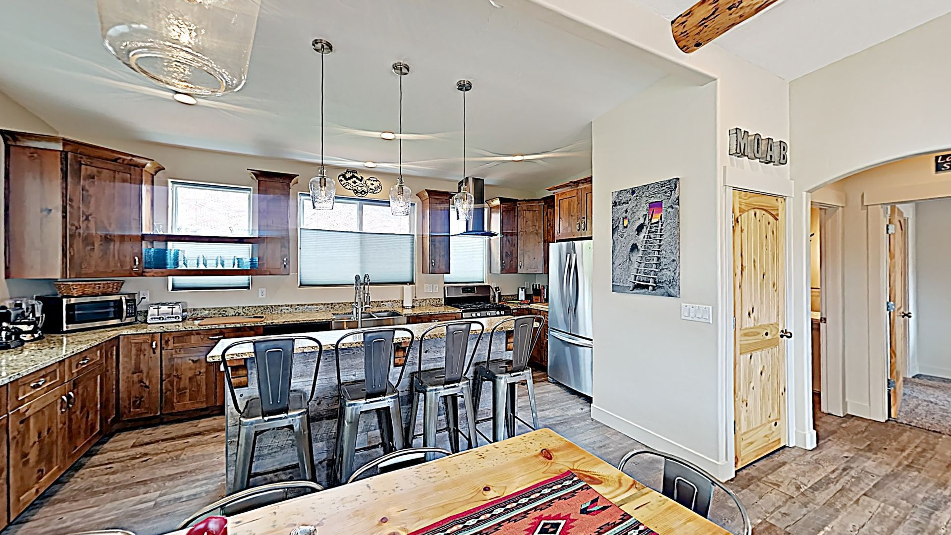 Village Place Moab vacation rental Kitchen with wooden cabinets, island with stools, and dining table.