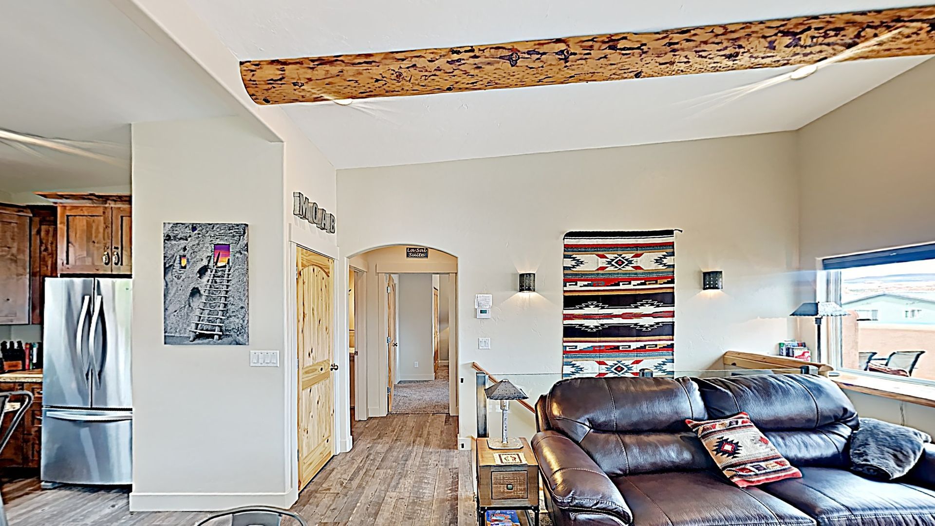 Village Place Moab vacation rental Living room with brown leather sofa, rug, wooden beam, and stainless steel refrigerator.