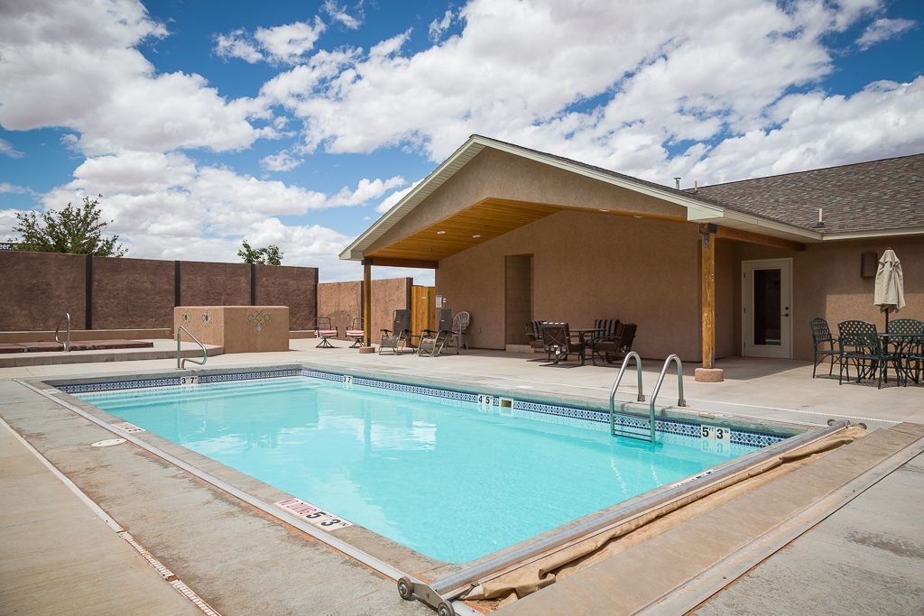 Pool with turquoise water, patio, and brown stucco building under a cloudy sky.