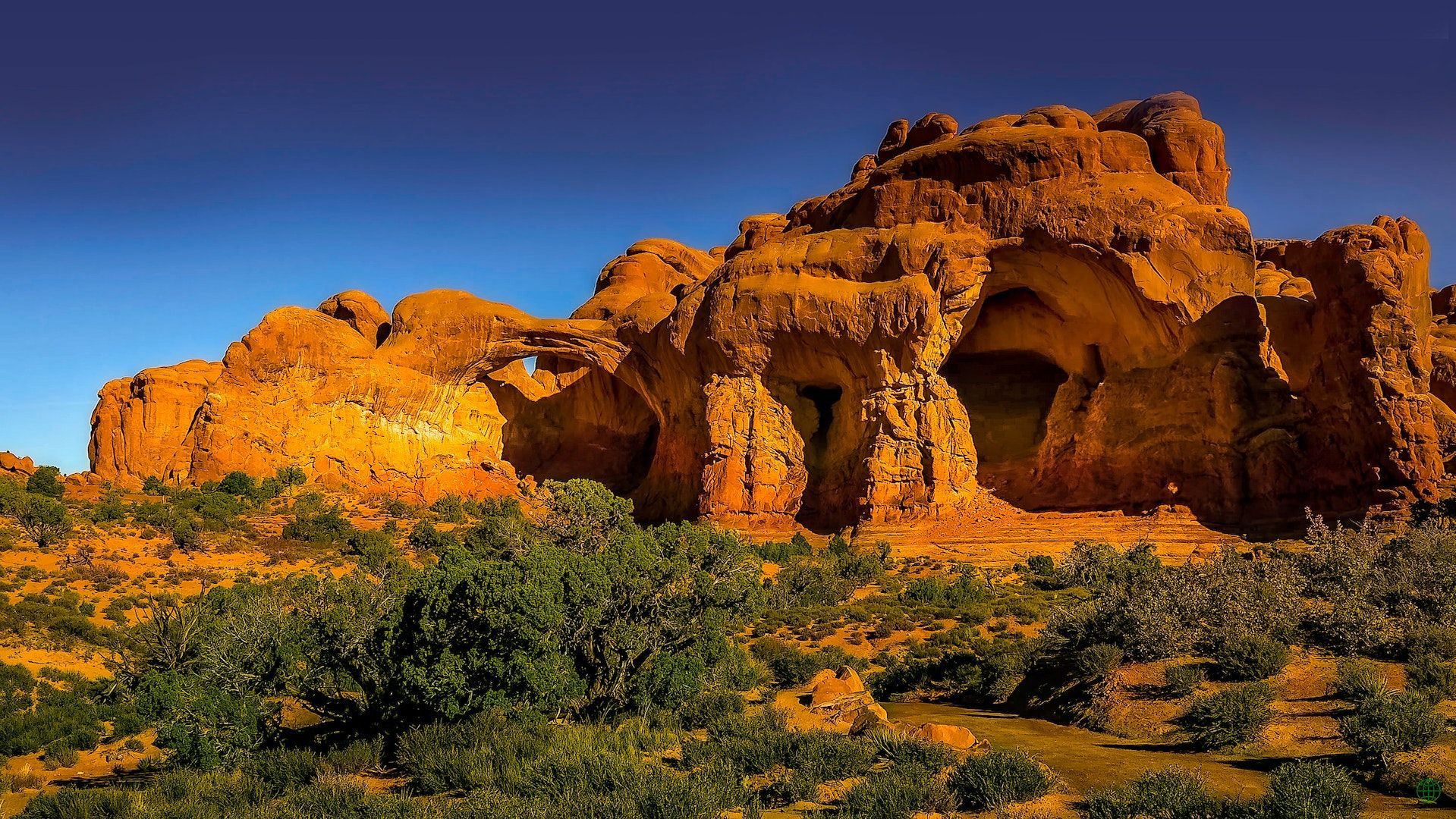 A large rock formation in the middle of a desert surrounded by trees.