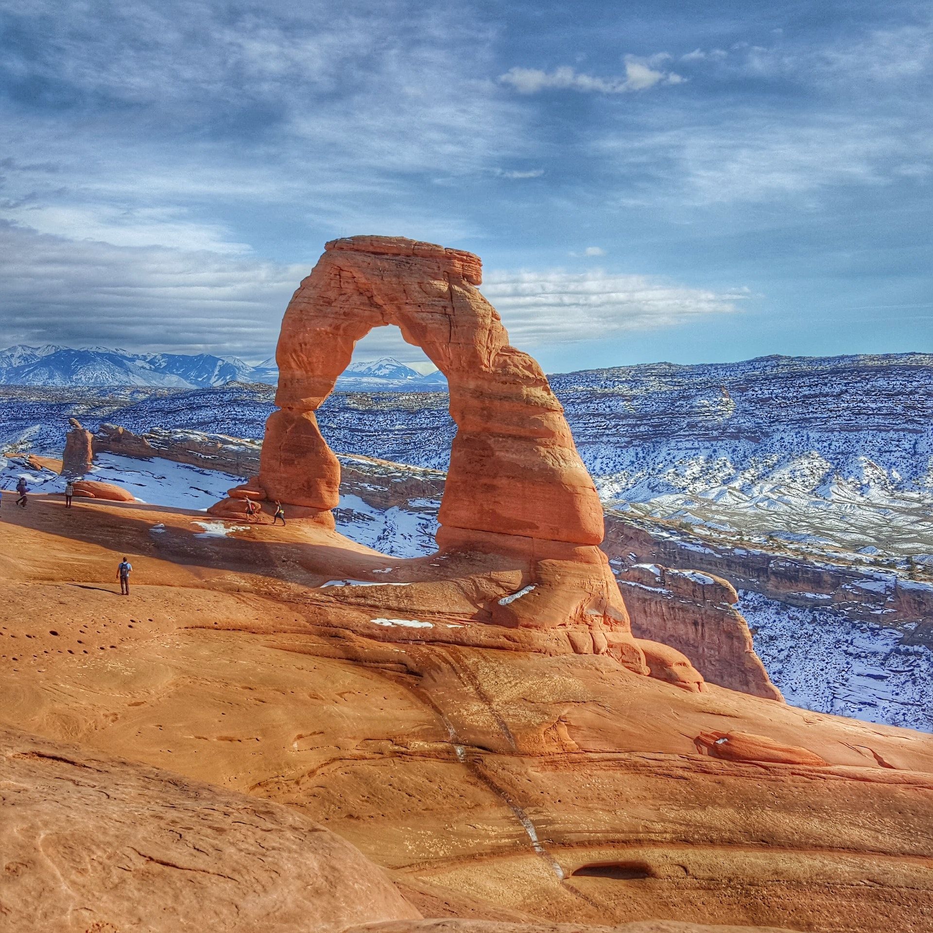 Delicate Arch in Arches National Park, Utah, with a snowy backdrop and a blue sky.