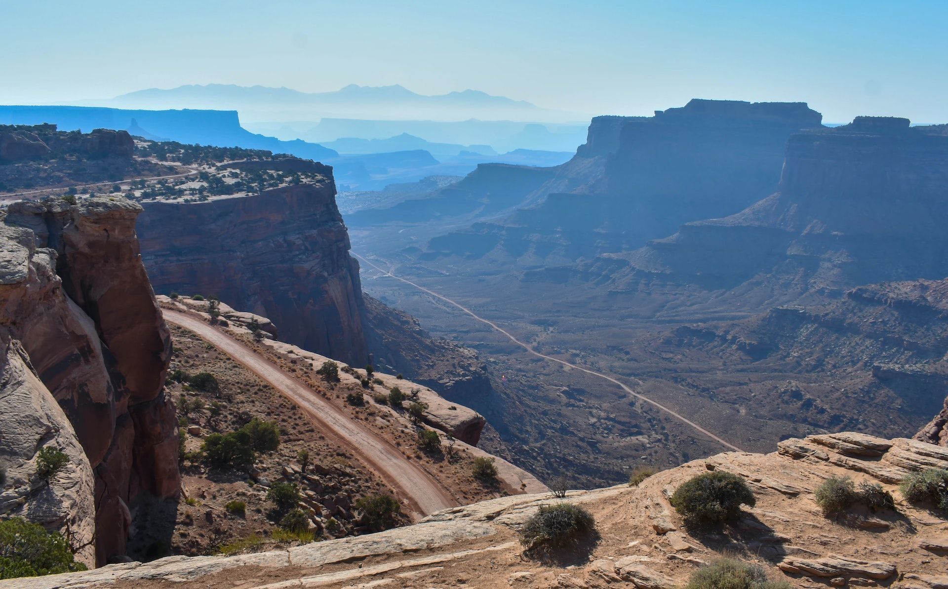 Scenic view of canyons and a winding dirt road in a desert landscape under a blue sky.