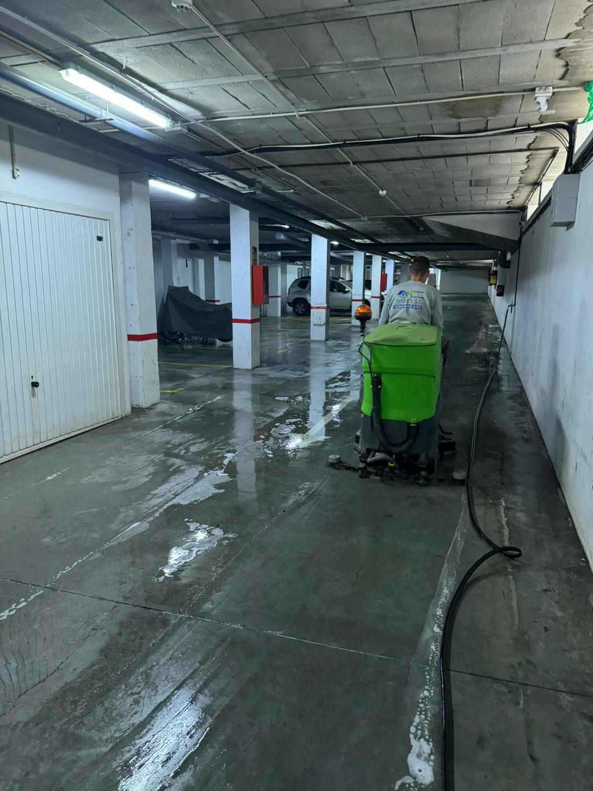 Una persona está limpiando un estacionamiento con una aspiradora verde.