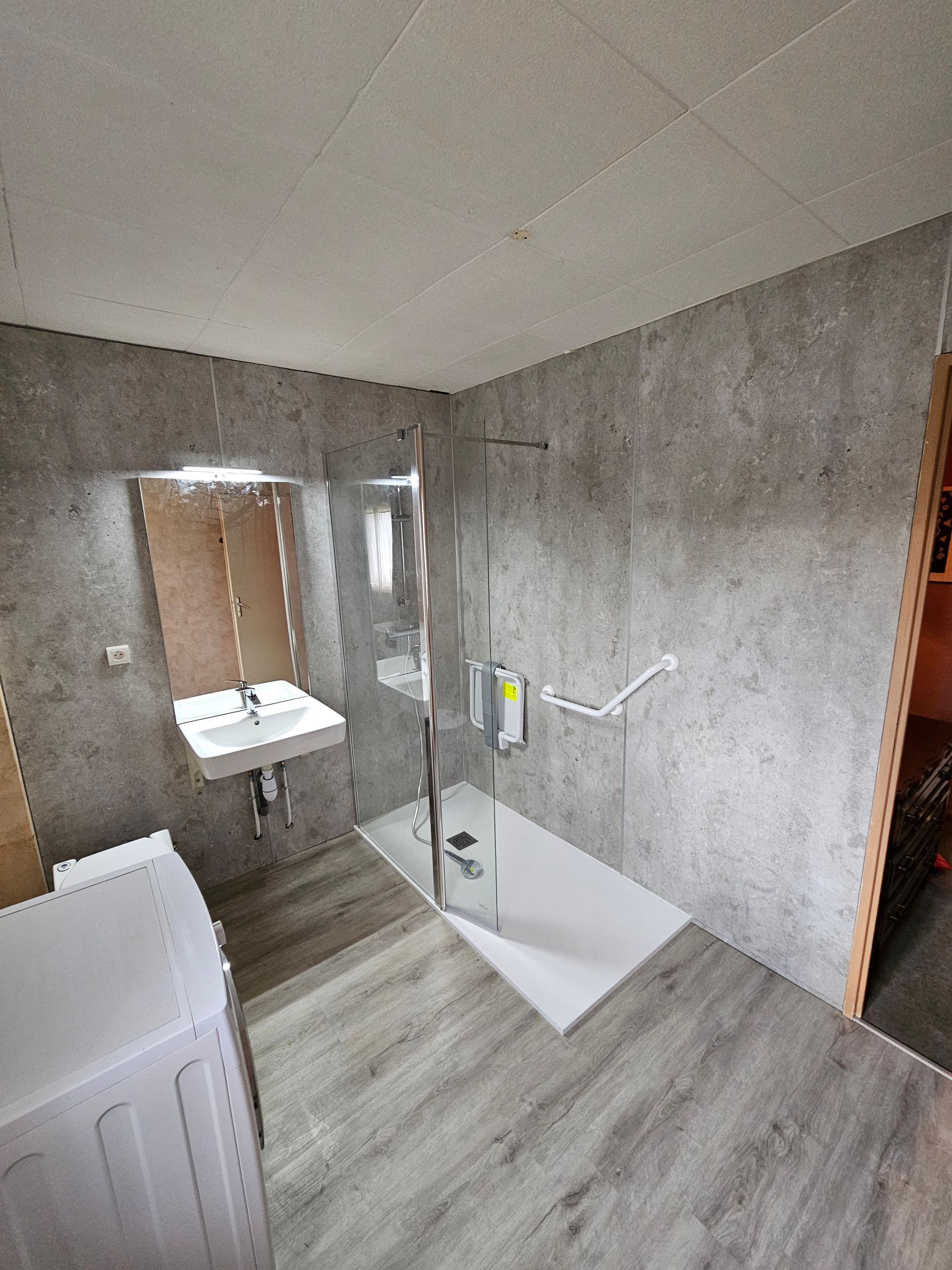 Salle de bains PMR avec barre de maintien, siège de douche rabattable et lavabo suspendu