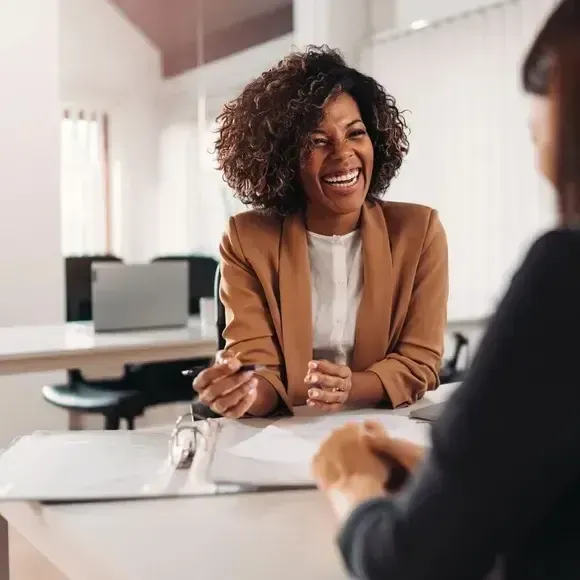 Uma mulher está sentada à mesa conversando com outra mulher.