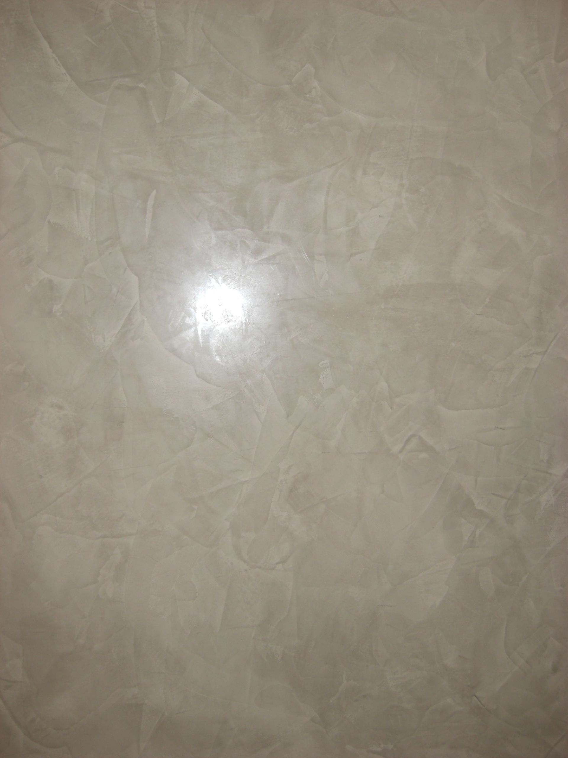 Mur texturé blanc cassé avec des motifs tourbillonnants et un reflet central lumineux.