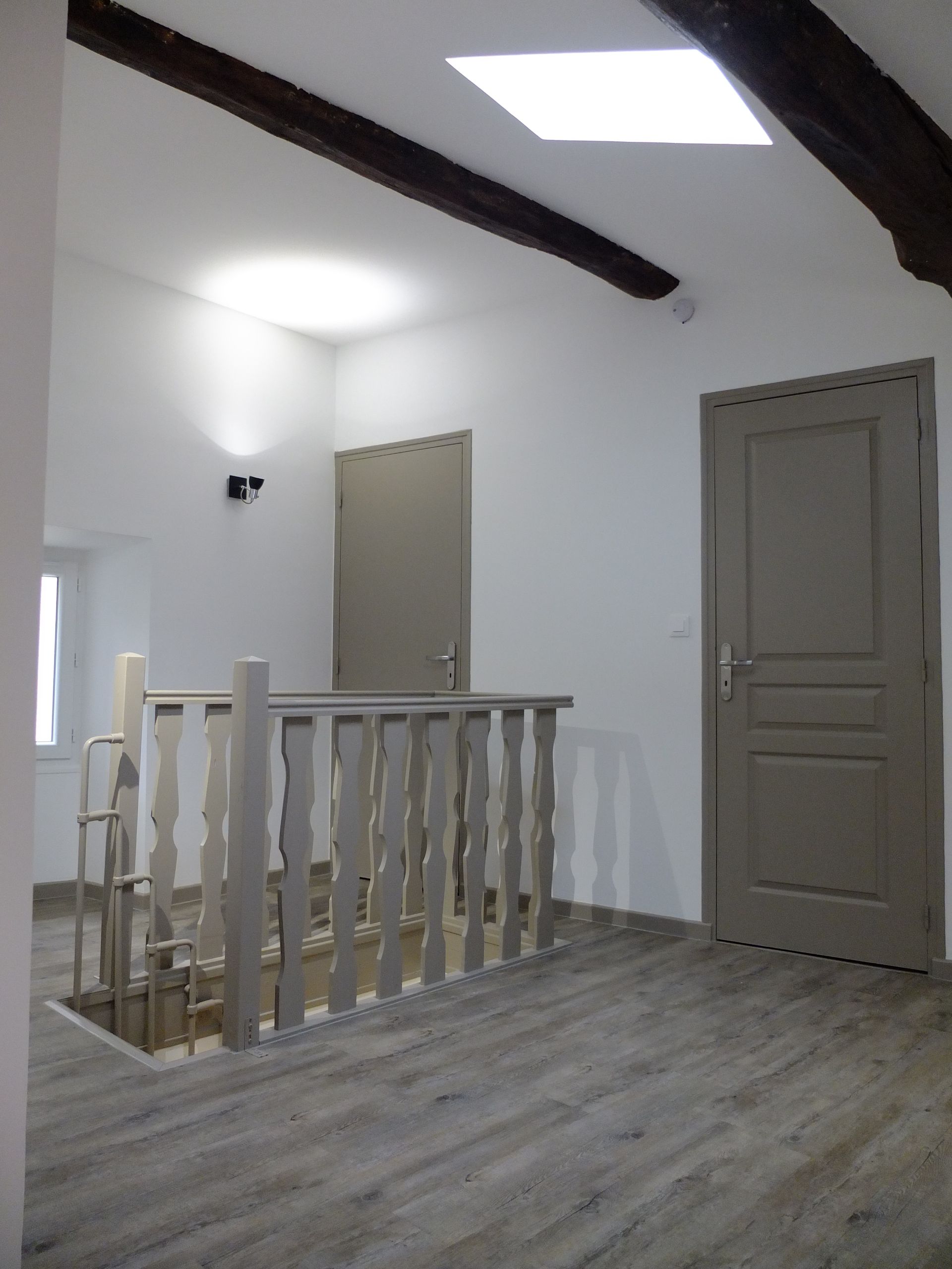 Couloir intérieur avec poutres en bois, portes grises et escalier avec rampe en bois.