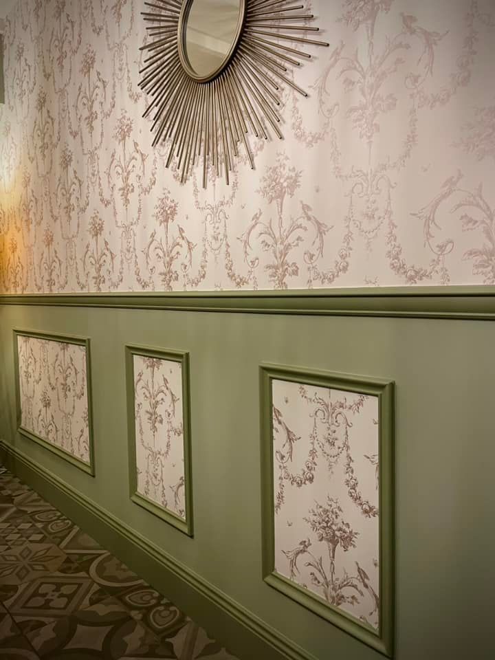 Couloir avec papier peint à motifs, miroir décoratif, panneaux encadrés.