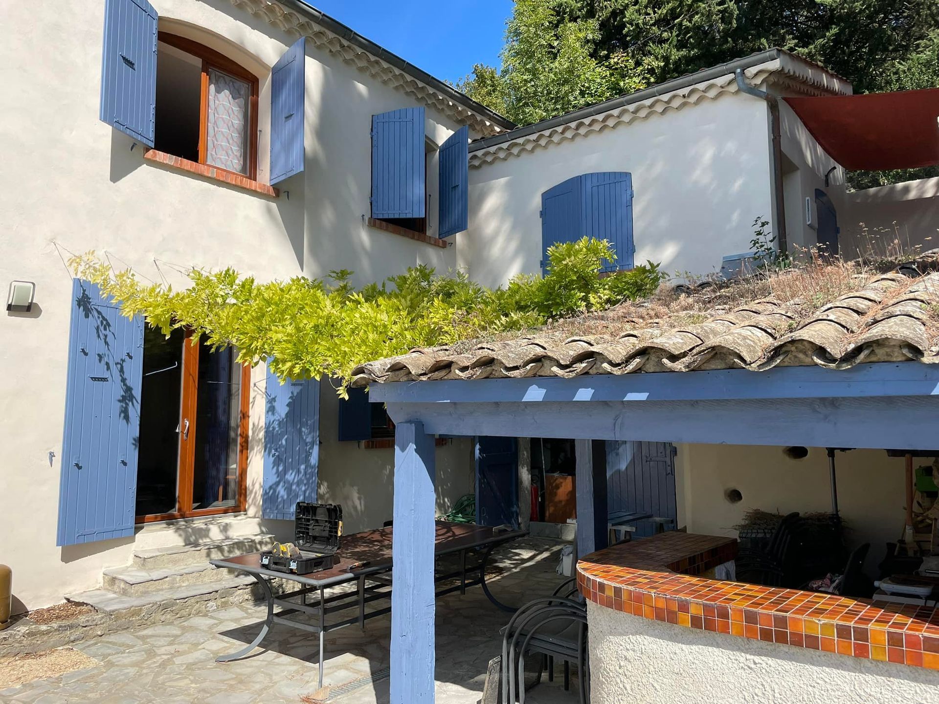 Maison à deux étages avec volets bleus, treillis blanc et balcon.