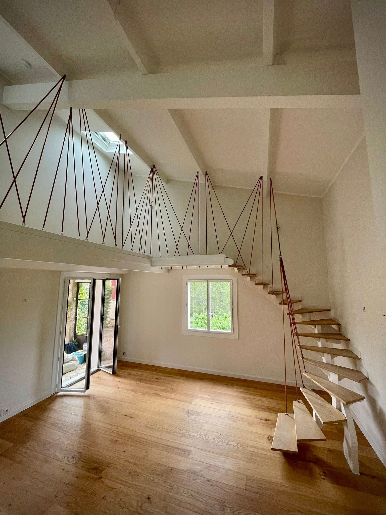 Toit de tuiles brunes recouvert de mousse, cheminée, branches d'arbres sur fond de ciel bleu.