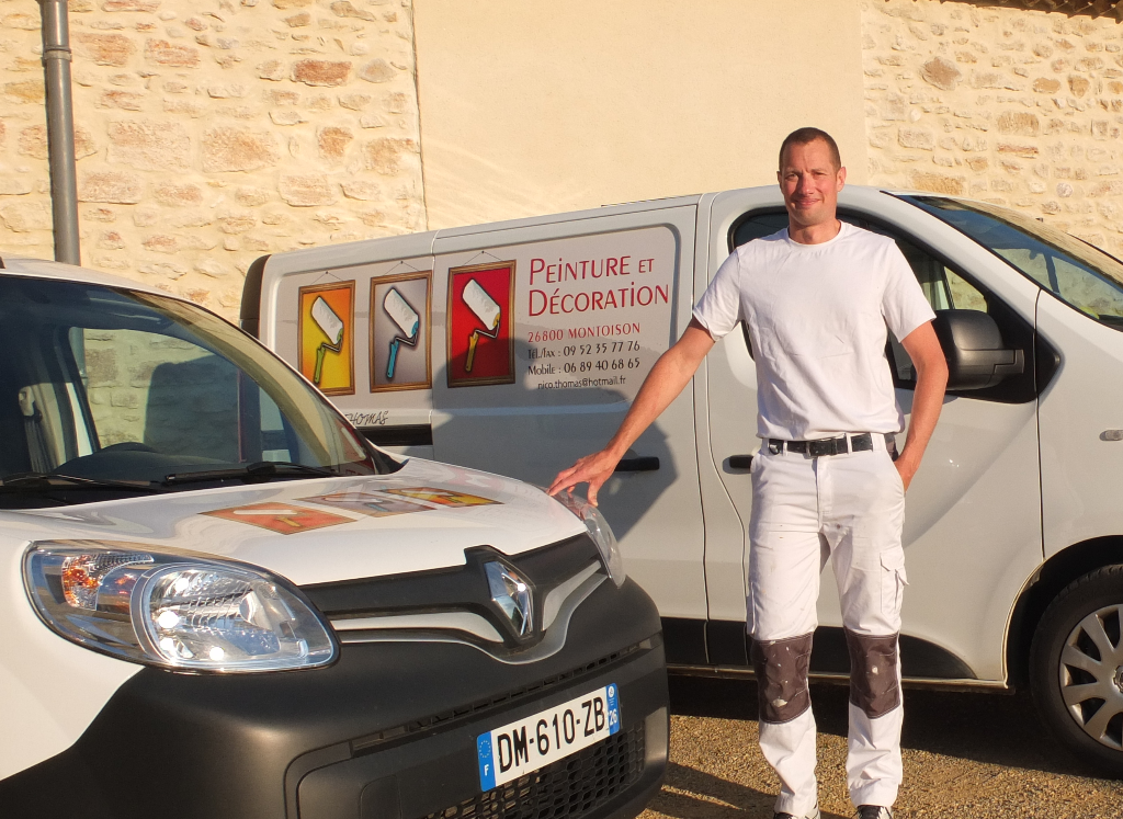 Monsieur THOMAS Nicolas en vêtements de travail blancs se tient près des véhicules de l'entreprise.