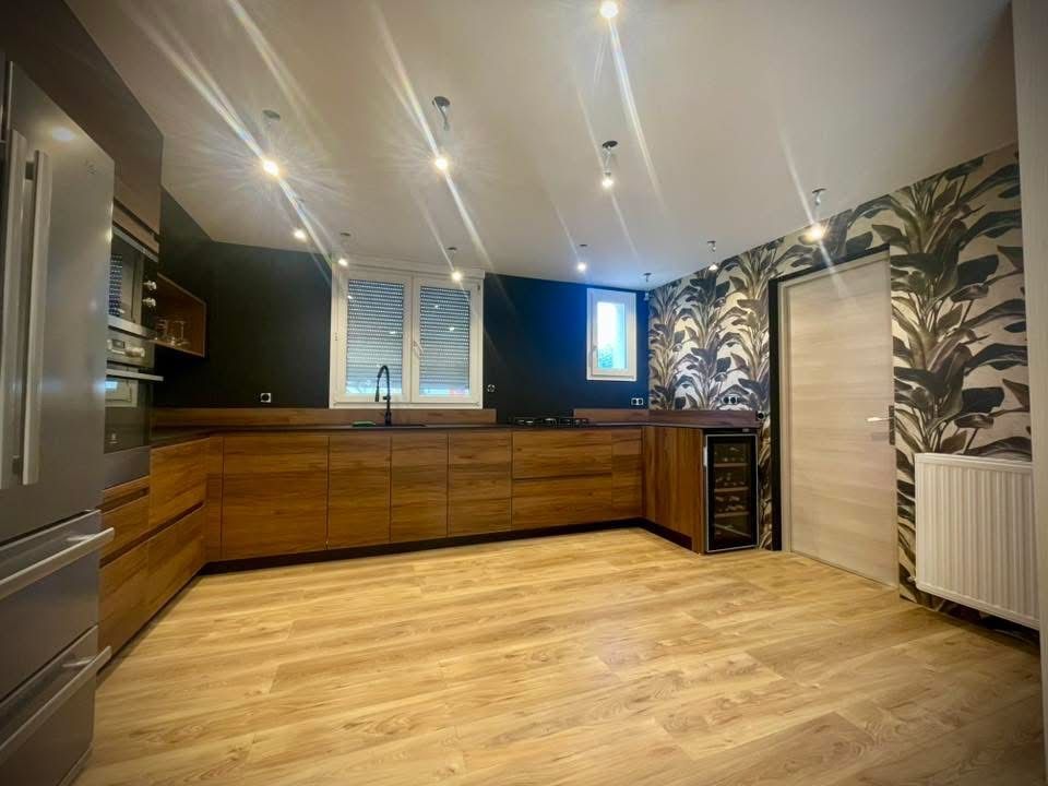 Cuisine moderne avec placards en bois, plans de travail noirs et papier peint à motifs.