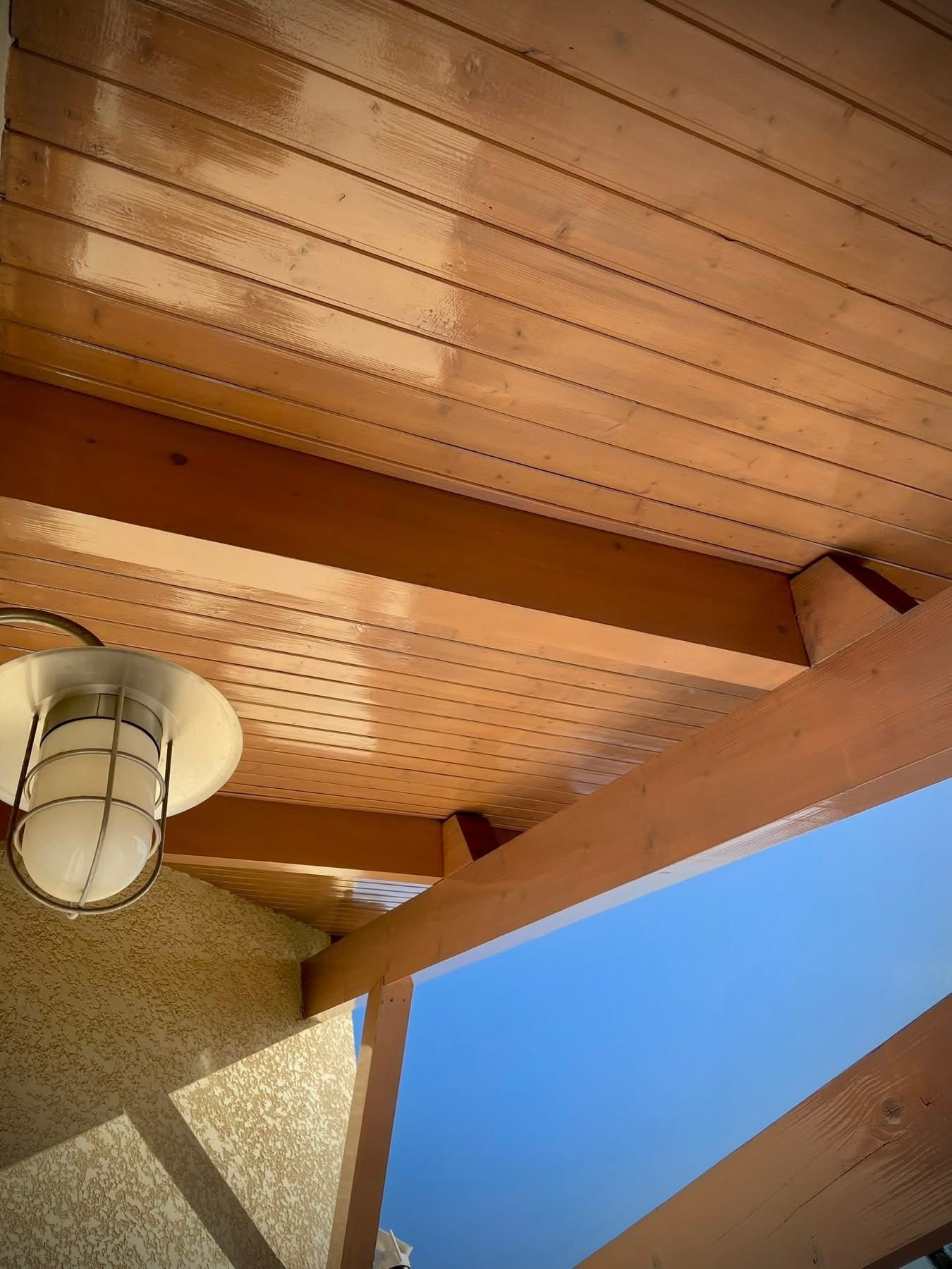 Plafond en bois avec luminaire, poutres et vue sur un ciel bleu.