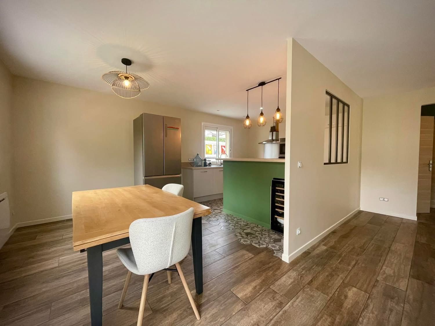 Coin repas avec table et chaises en bois, attenant à une cuisine avec un mur d'accent vert.