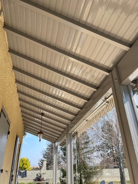 Plafond de véranda beige et gris avec poutres et lambris, offrant une vue sur l'extérieur.