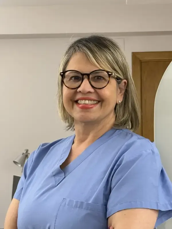 Una mujer con uniforme azul y gafas sonríe a la cámara.