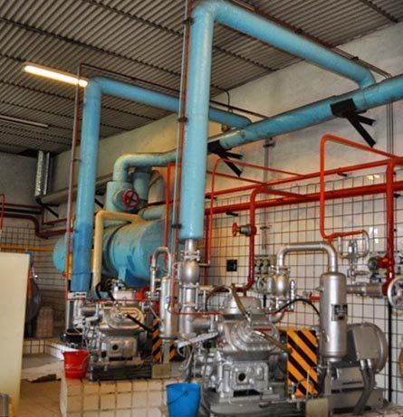Equipo de refrigeración industrial con tuberías azules y maquinaria plateada en una sala embaldosada.