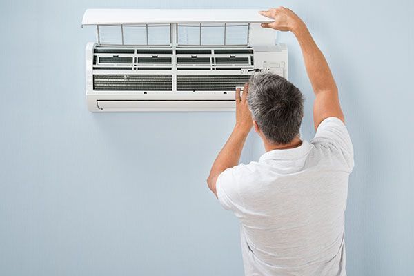 Hombre abriendo el aire acondicionado para inspeccionar el filtro. Contra una pared azul claro.