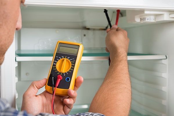 Hombre usando un multímetro dentro de un refrigerador para probar componentes eléctricos.
