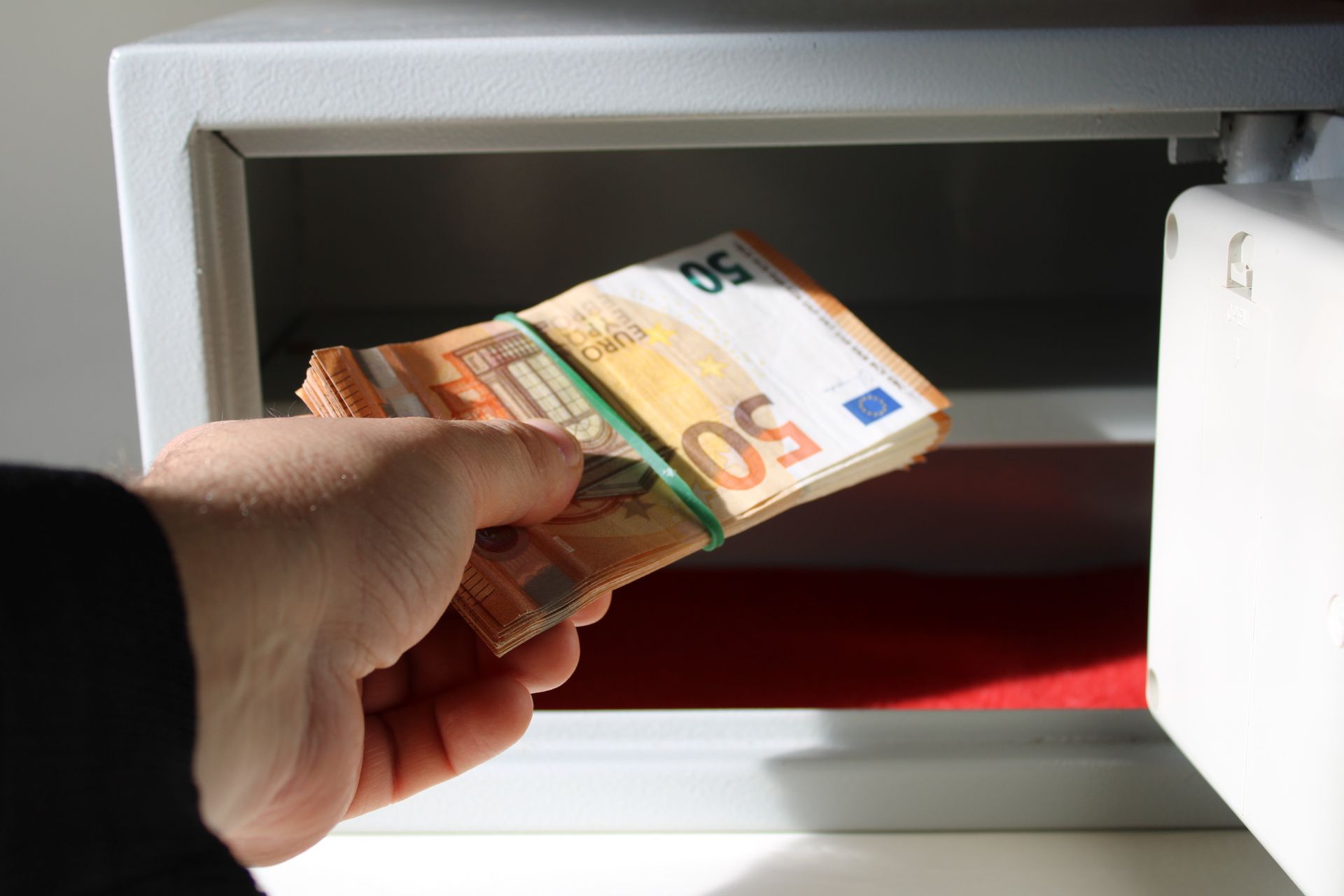 Personne déposant une liasse de billets de 50 euros dans un coffre-fort