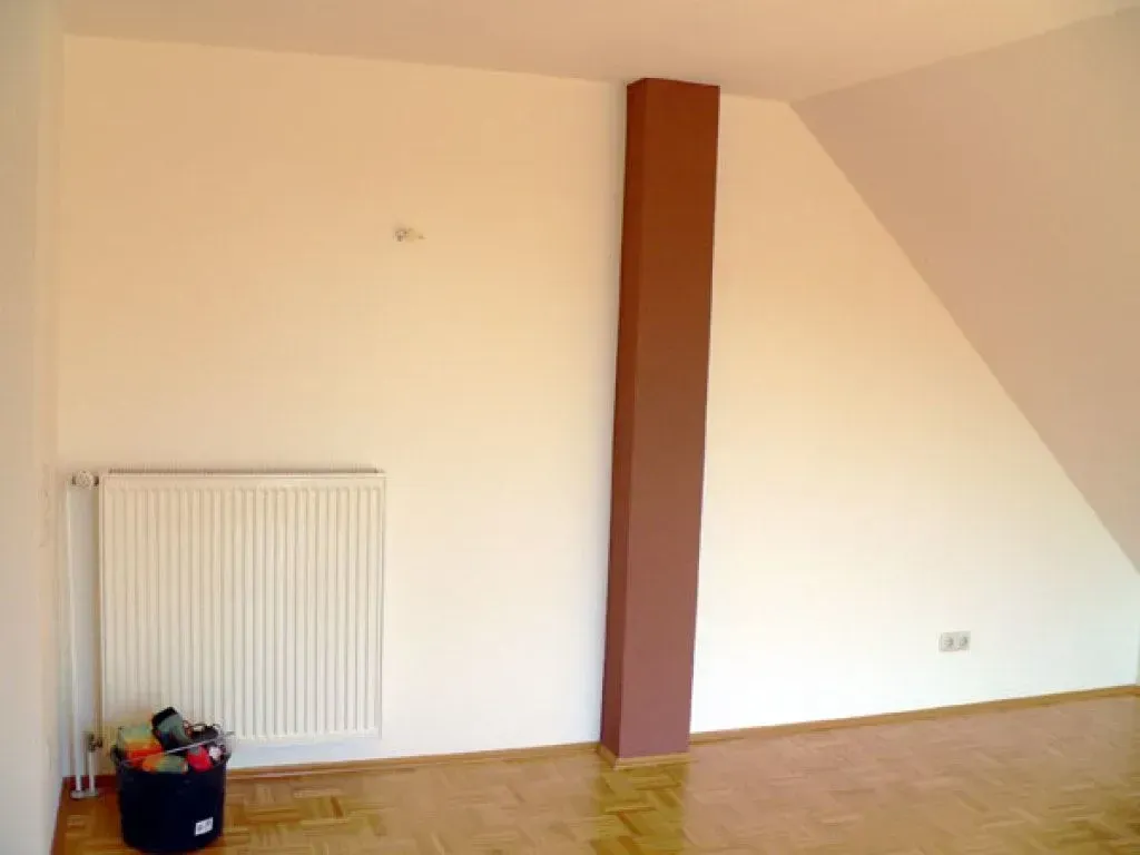 Ein leerer Raum mit einem weißen Heizkörper und einer rot-braunen Säule