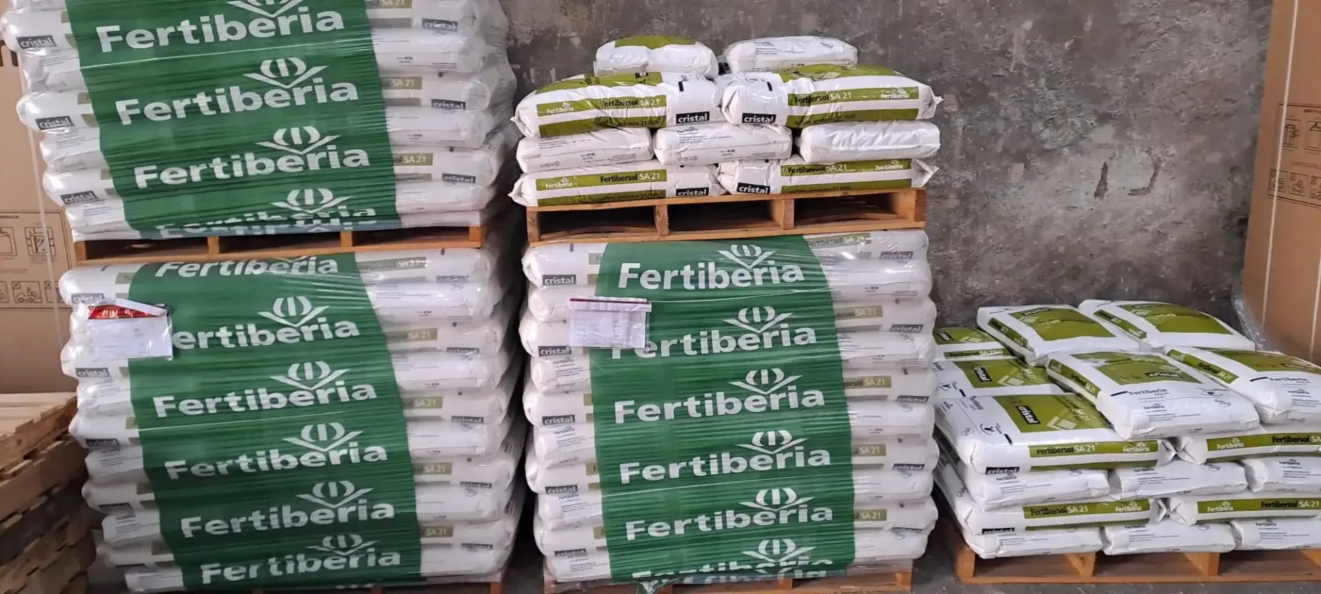 Tres palets de madera apilados con sacos de fertilizante Fertiberia blancos y verdes en un almacén.