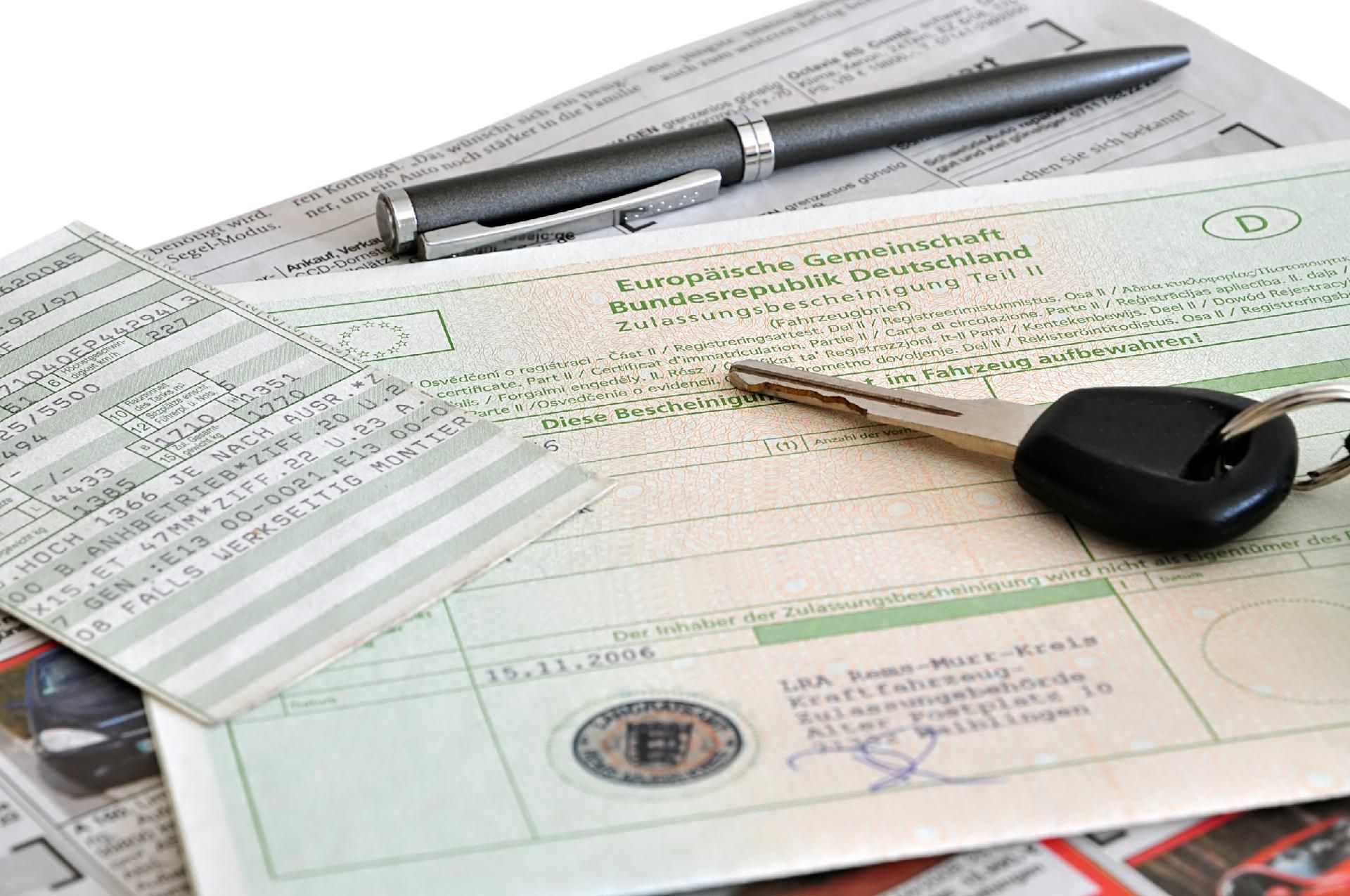 Autoschlüssel, Papiere und ein Stift auf einem Stapel Dokumente, wahrscheinlich im Zusammenhang mit der Fahrzeugzulassung.