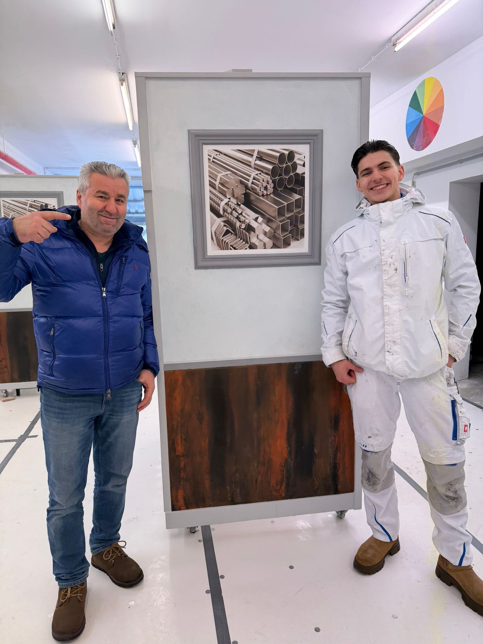 Zwei Personen stehen vor einem gerahmten Schwarz-Weiß-Architekturbild, das an einer Wand in einem hellen, modernen Studio hängt.