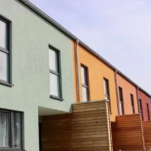 Eine Reihe von Stadthäusern, jedes in einer anderen Farbe: grün, orange und rot, mit Holzelementen.