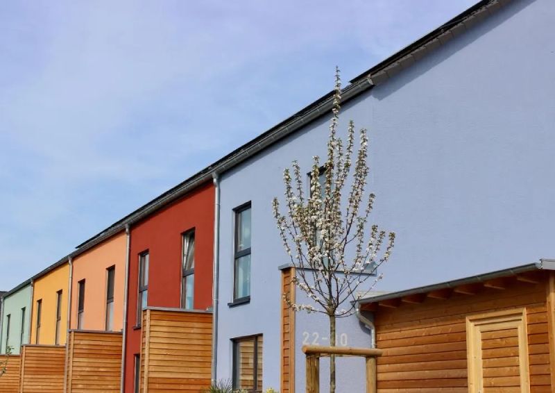 Eine Reihe bunter Stadthäuser mit Holzzäunen unter blauem Himmel.