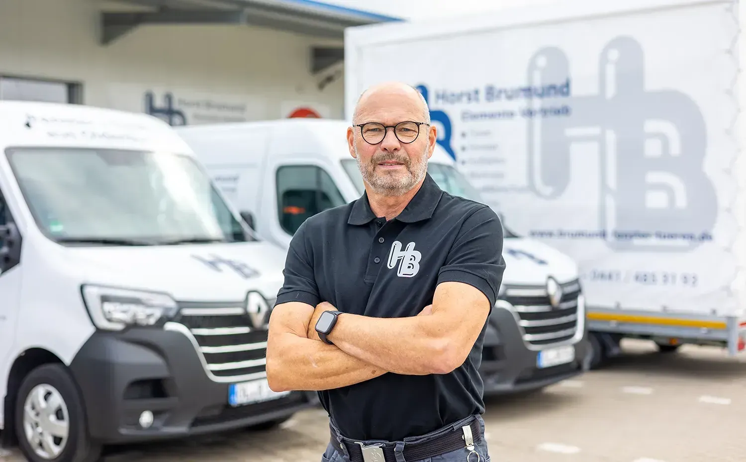 Ein Mann steht mit verschränkten Armen vor einer Reihe von Lieferwagen.