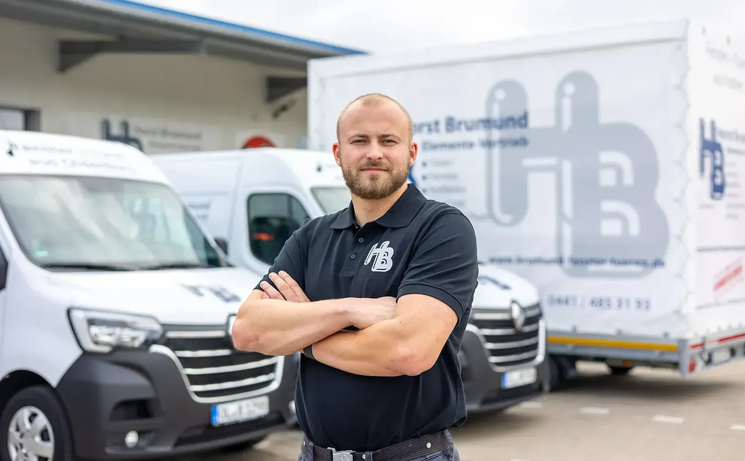 Ein Mann steht mit verschränkten Armen vor einer Reihe von Lieferwagen.